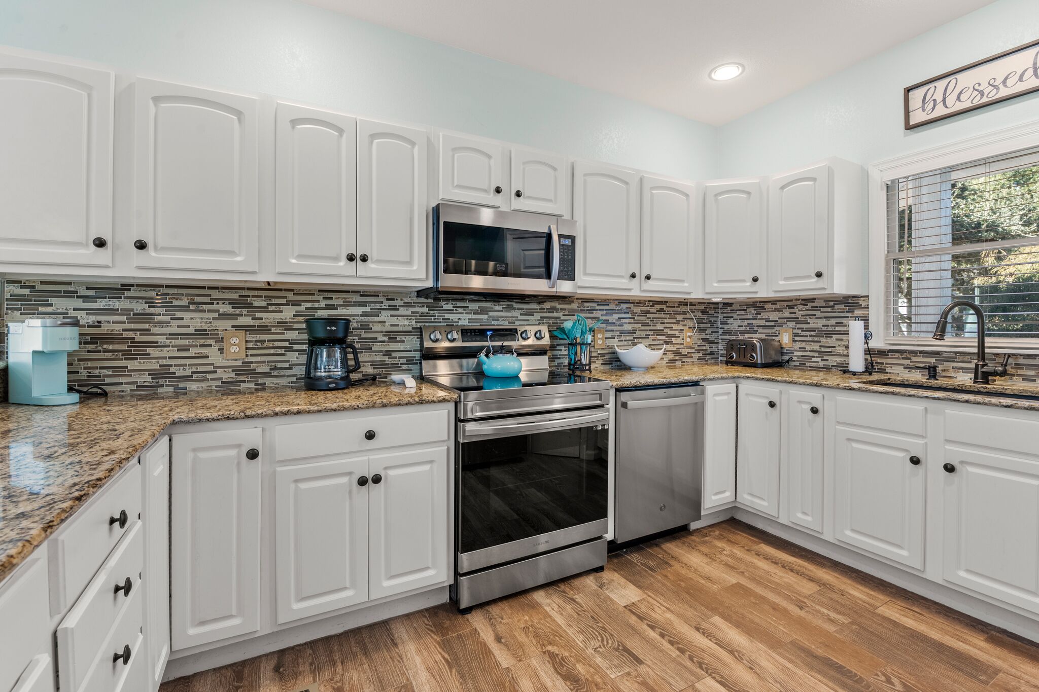 A modern kitchen with white cabinetry, a stainless steel microwave, a built-in oven, and a coffee maker.