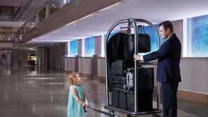 A man in a suit interacting with a luggage cart in a spacious, modern hotel lobby with a high ceiling and a polished floor.