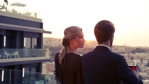 A couple overlooking a cityscape from a balcony with a clear view of the buildings below.