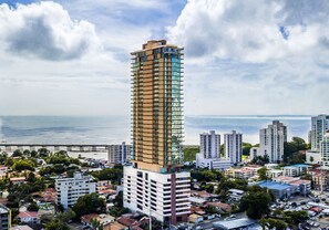 A high-rise building with multiple floors, surrounded by other buildings and a coastal view.