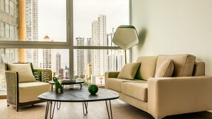 A modern living room with a large window, a beige sofa, a smaller armchair, and a round coffee table with decorative items. - Panoramic Apartment Ocean View (Panama City)