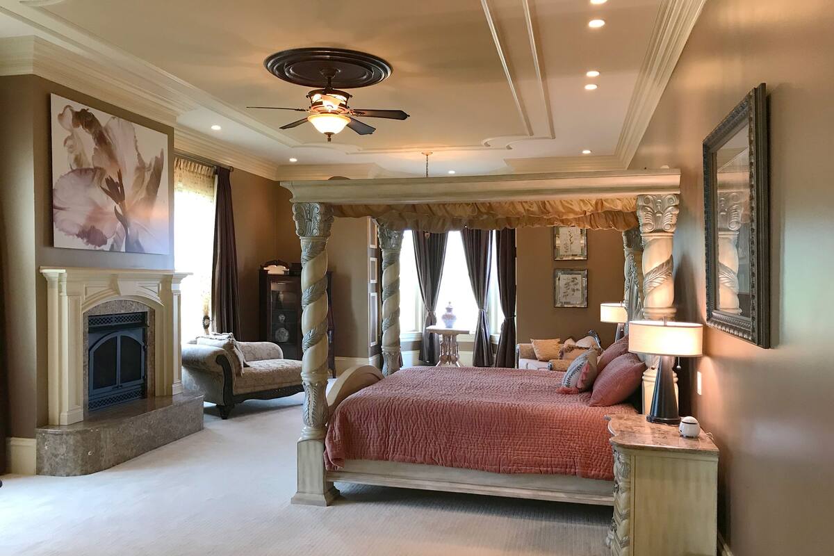 A spacious bedroom with a large bed, a fireplace, and a ceiling fan.