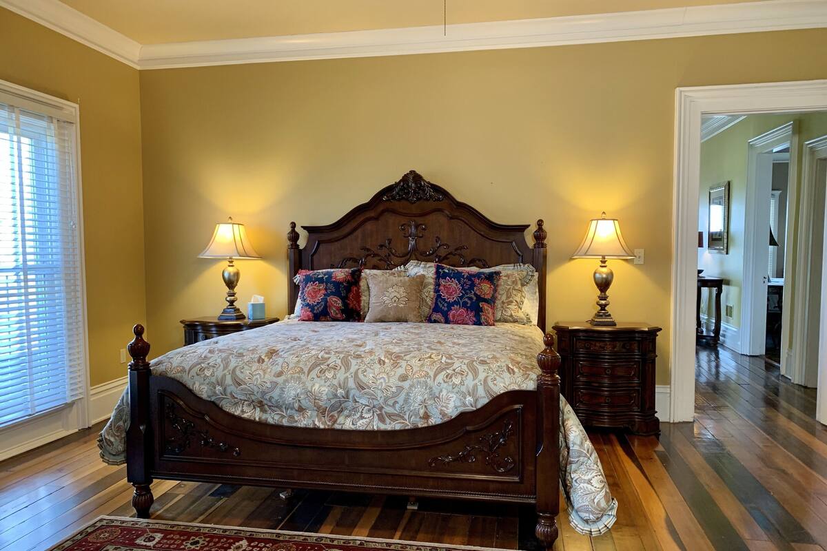 A bedroom with a large bed, two bedside tables with lamps, a wooden headboard, and a patterned rug.
