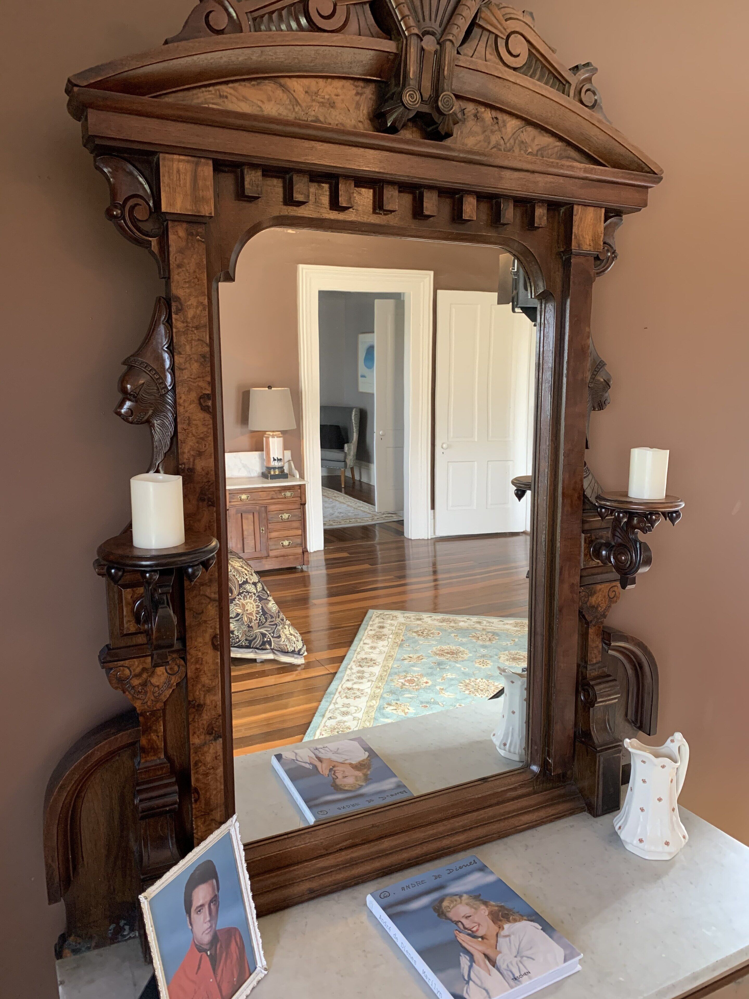 A room with a large ornate mirror, wooden furniture, a rug, and framed photographs.