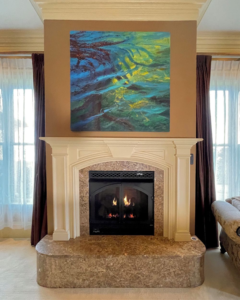 A fireplace with a stone surround, a painting above it, and curtains on the windows.
