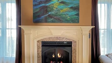 A fireplace with a stone surround, a painting above it, and curtains on the windows.