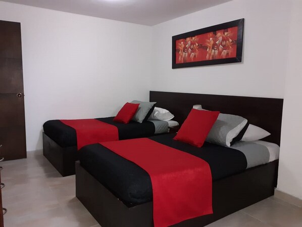 Un dormitorio con dos camas, cada una con ropa de cama roja y gris, un cabecero oscuro y un cuadro en la pared.