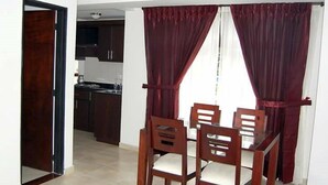 A dining area with a table and chairs, a kitchen in the background, and red curtains. - Gran Hotel Coral (Popayán)