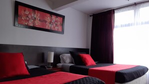A hotel room with two beds, each with red and black bedding, a nightstand with a lamp, and a painting on the wall. - Gran Hotel Coral (Popayán)