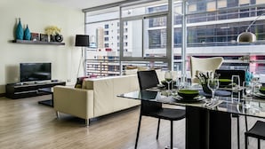 Un salon moderne comprenant un canapé, un téléviseur et un coin repas avec une table en verre.