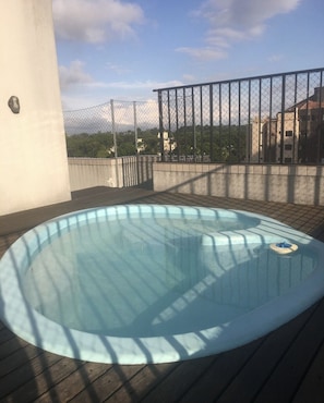 Un bain à remous sur une terrasse en bois, avec en arrière-plan des bâtiments et des arbres.