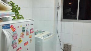 A kitchen with a refrigerator covered in magnets, a washing machine, and a window with a view of the outside. - La Macarena 2001 (Bogotá)
