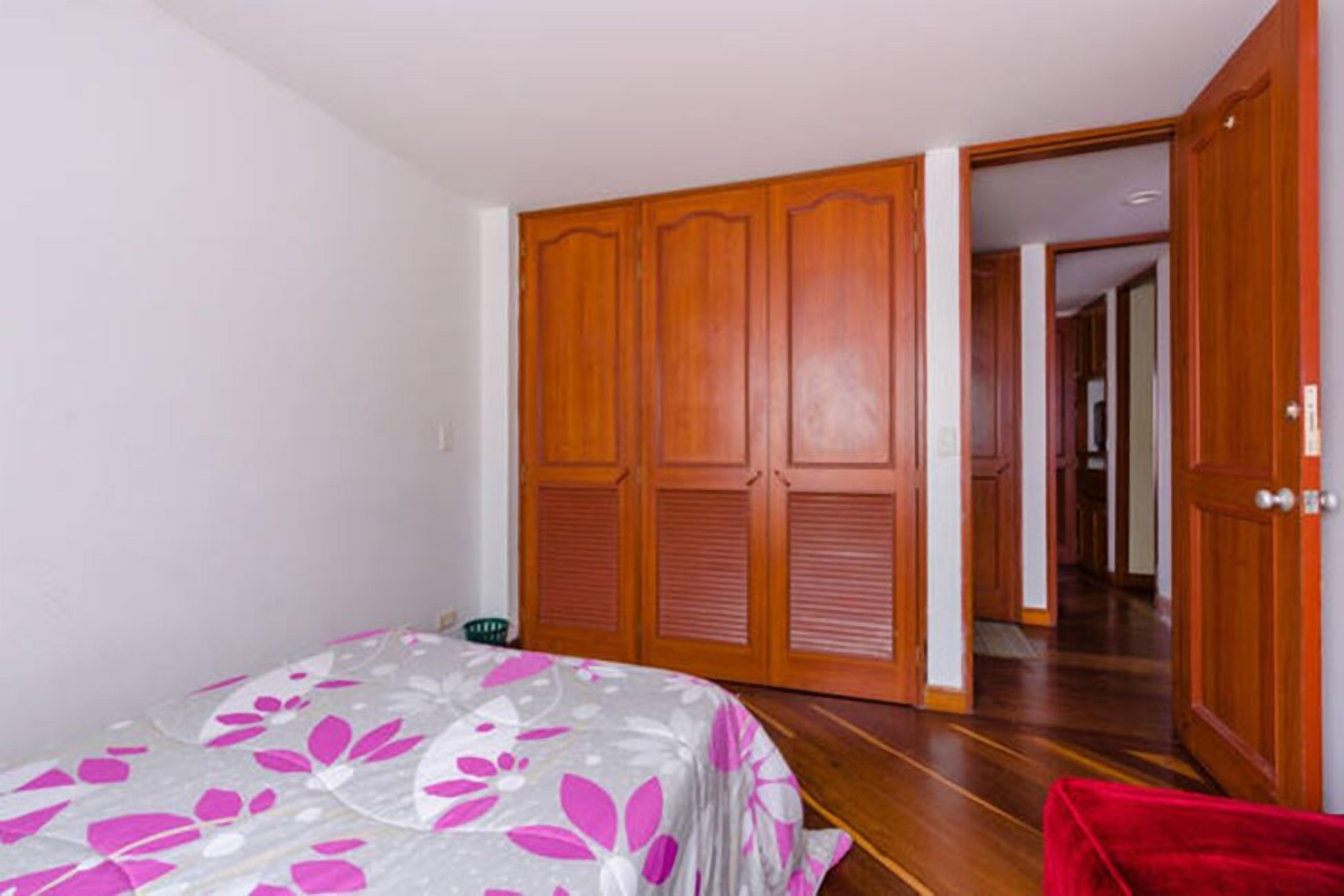 Un dormitorio con cama, armario de madera y una silla roja.