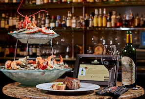 A seafood platter with shrimp and oysters, a bottle of wine, and a framed menu on a bar counter.