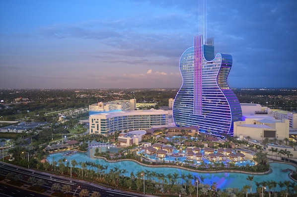 A hotel with a guitar-shaped building, a large pool, and surrounding greenery.