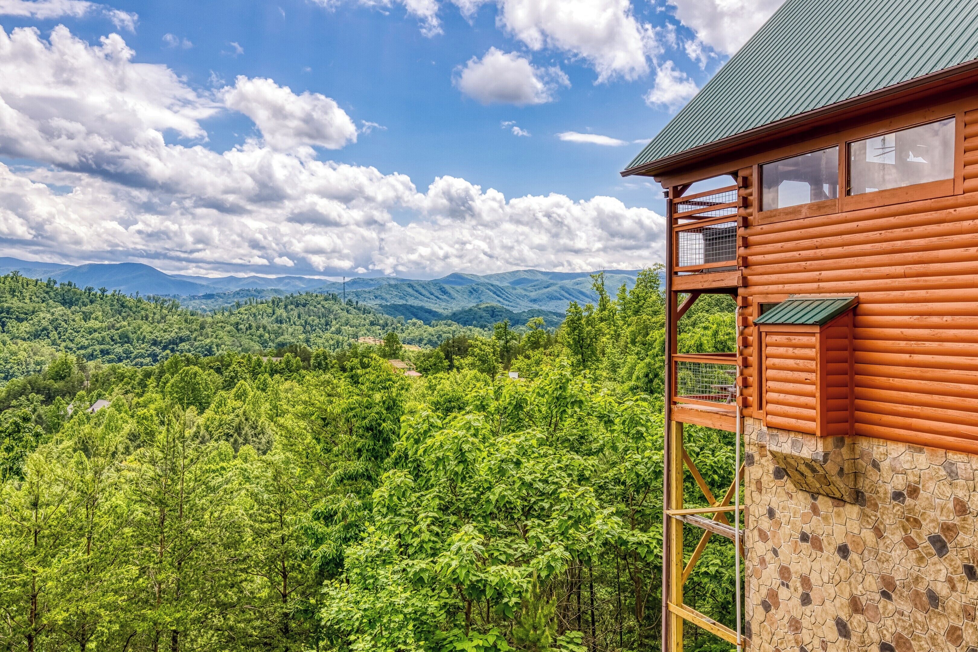 Una cabaña de madera con balcón que da a un valle boscoso y montañas distantes.