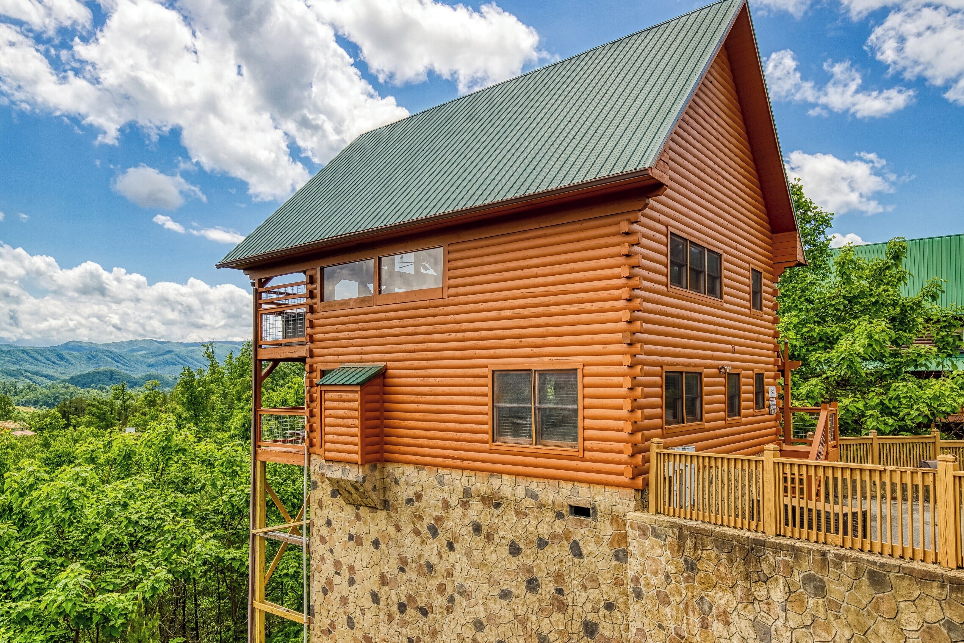 A log cabin with a stone foundation, a balcony, and a view of mountains.