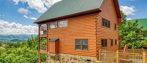 A log cabin with a stone foundation, a balcony, and a view of mountains.