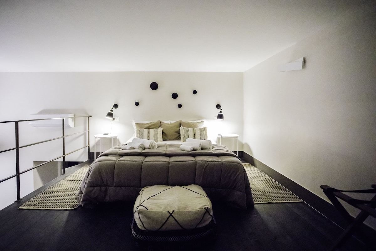 A neatly arranged bedroom with a bed, bedside lamps, a small table, and a bench.