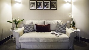 Un sofá de color neutro con cojines estampados, un jarrón con flores blancas y cuadros en la pared.