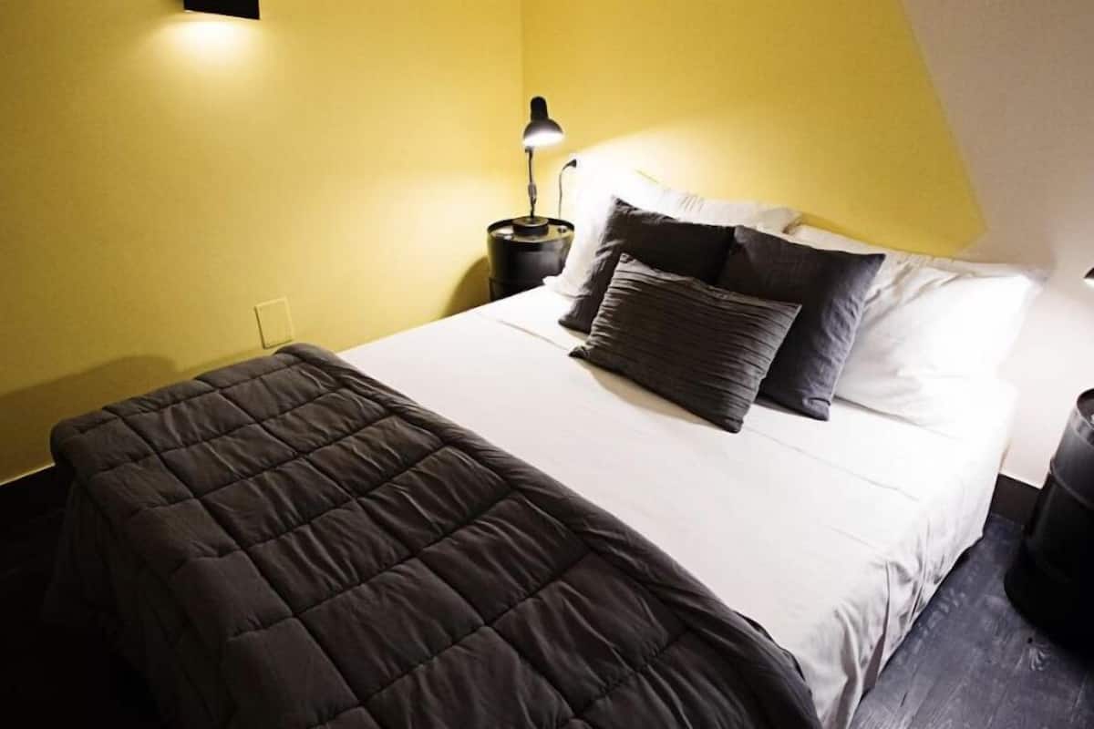A neatly made bed with a dark quilt, a bedside lamp, and a nightstand.
