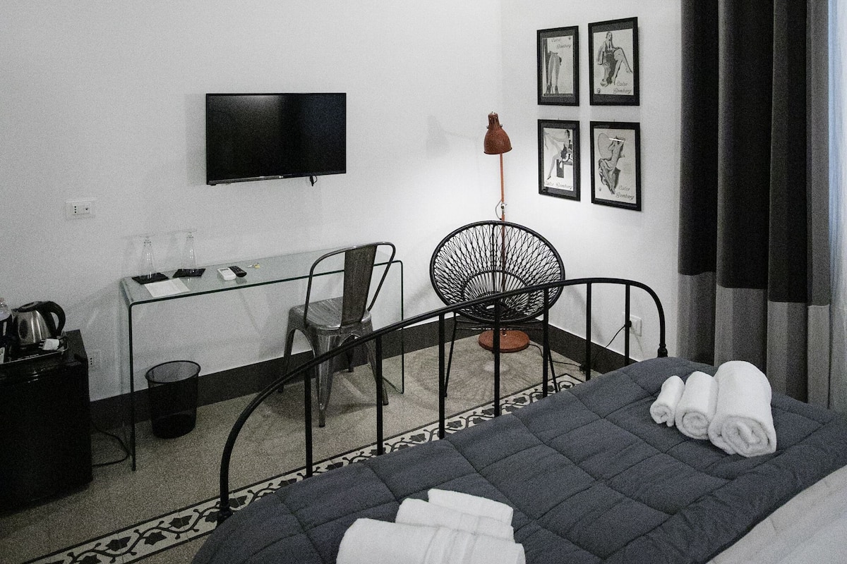 A modern hotel room with a bed, a desk, a chair, and a TV.