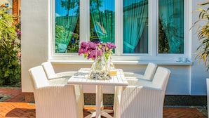 A white wicker outdoor seating area with a table, chairs, and a vase of flowers.
