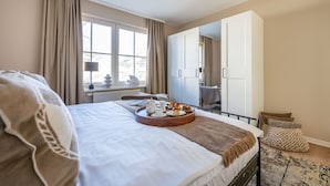 A hotel room with a bed, breakfast tray, window, wardrobe, and a view of the city.