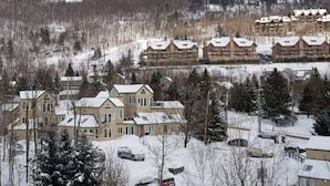 Ein Resort mit mehreren Gebäuden, darunter ein großes Lodgehaus und einige kleinere Blockhäuser, umgeben von schneebedeckten Bäumen und einer hügeligen Landschaft.