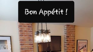 Ein Essbereich mit Kamin aus Ziegelsteinen, einem darüber montierten Fernseher und einem für vier Personen gedeckten Tisch mit Weingläsern und Tellern.