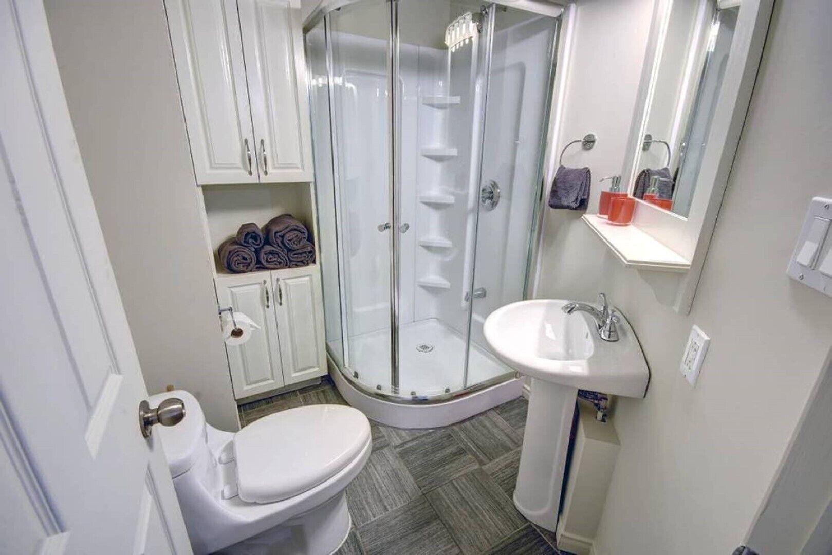 A bathroom with a toilet, a glass-enclosed shower, a sink, and a mirror.