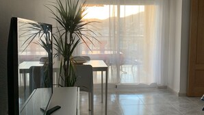 A modern living room with a flat-screen TV, a potted plant, a dining table, and a large window with sheer curtains. - Beachfront apartment with spectacular views
About this space (Oropesa del Mar (Castellón))