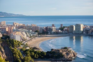 A coastal cityscape with a beach, buildings, and a rocky outcrop.