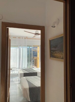 Una habitación con cama, ventilador de techo y vista a un balcón con barandilla.