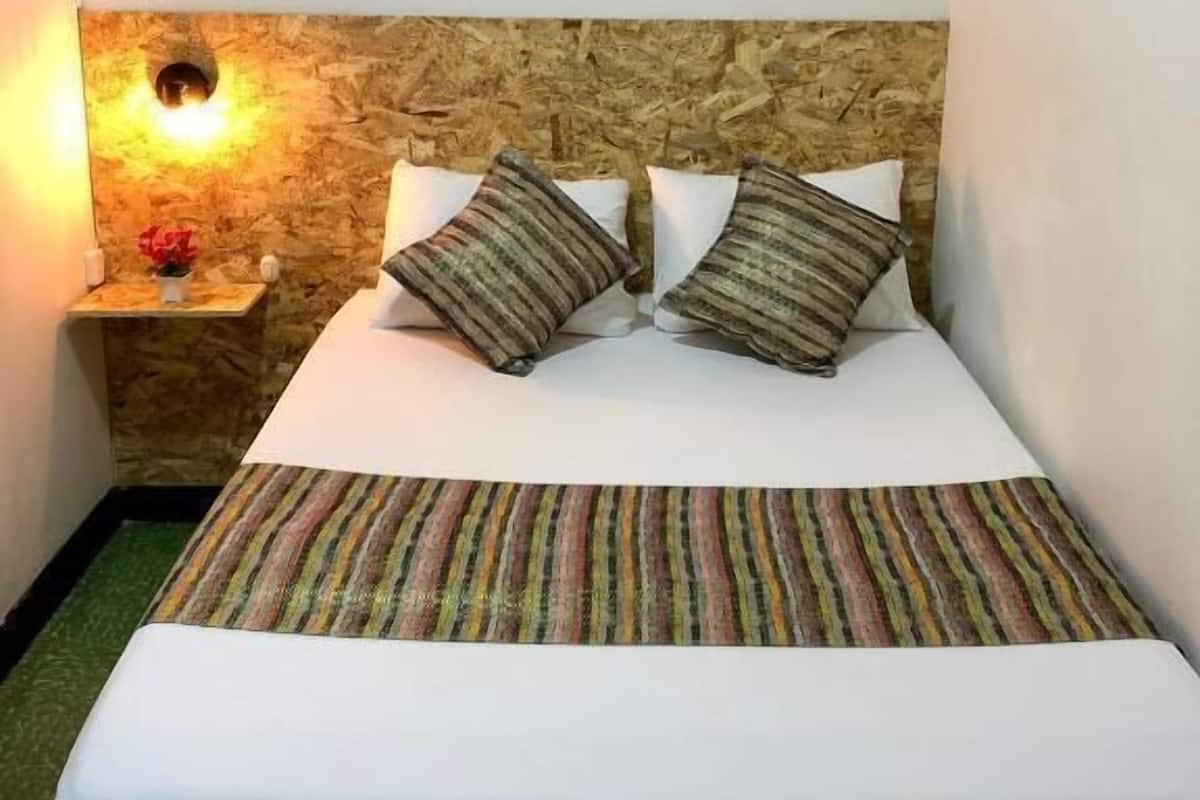 A hotel room with a bed, a nightstand with a lamp, and three framed pictures on the wall.