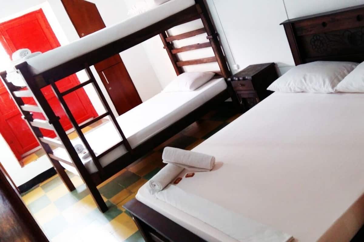 A single bed with white linens and a wooden headboard, a nightstand, and a red door in the background.