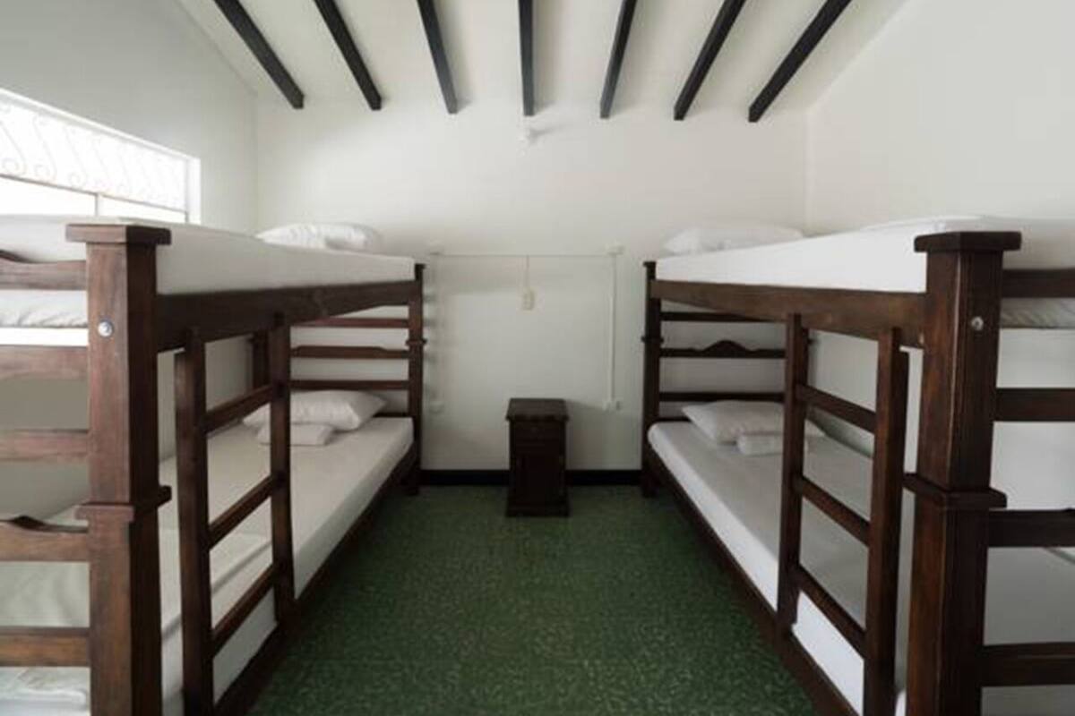 A dormitory room with bunk beds, a small bedside table, and a window.