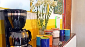 A coffee maker on a counter with colorful mugs and a vase of flowers. - Traveler Hostel (San Gil)
