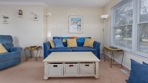A living room with a blue sofa, a white coffee table, wicker baskets, and a white brick wall.