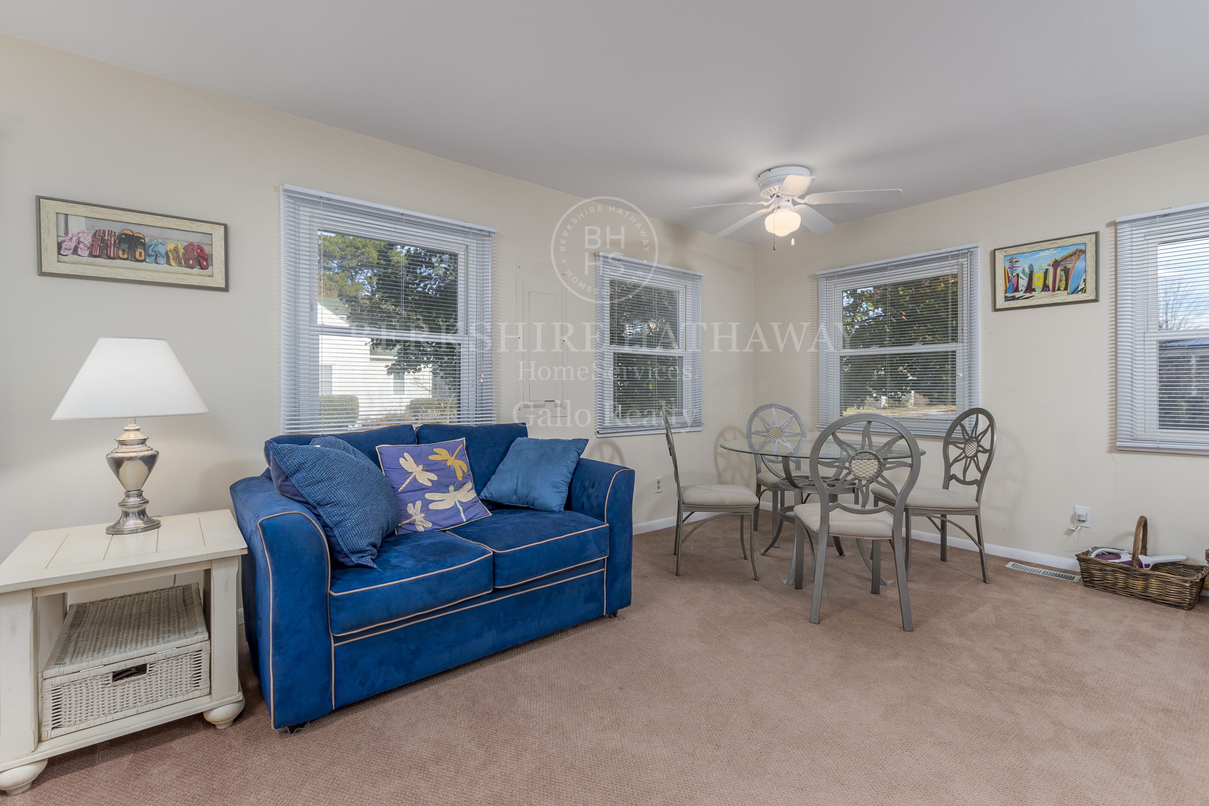 A living room with a blue sofa, a small table with chairs, and a ceiling fan.