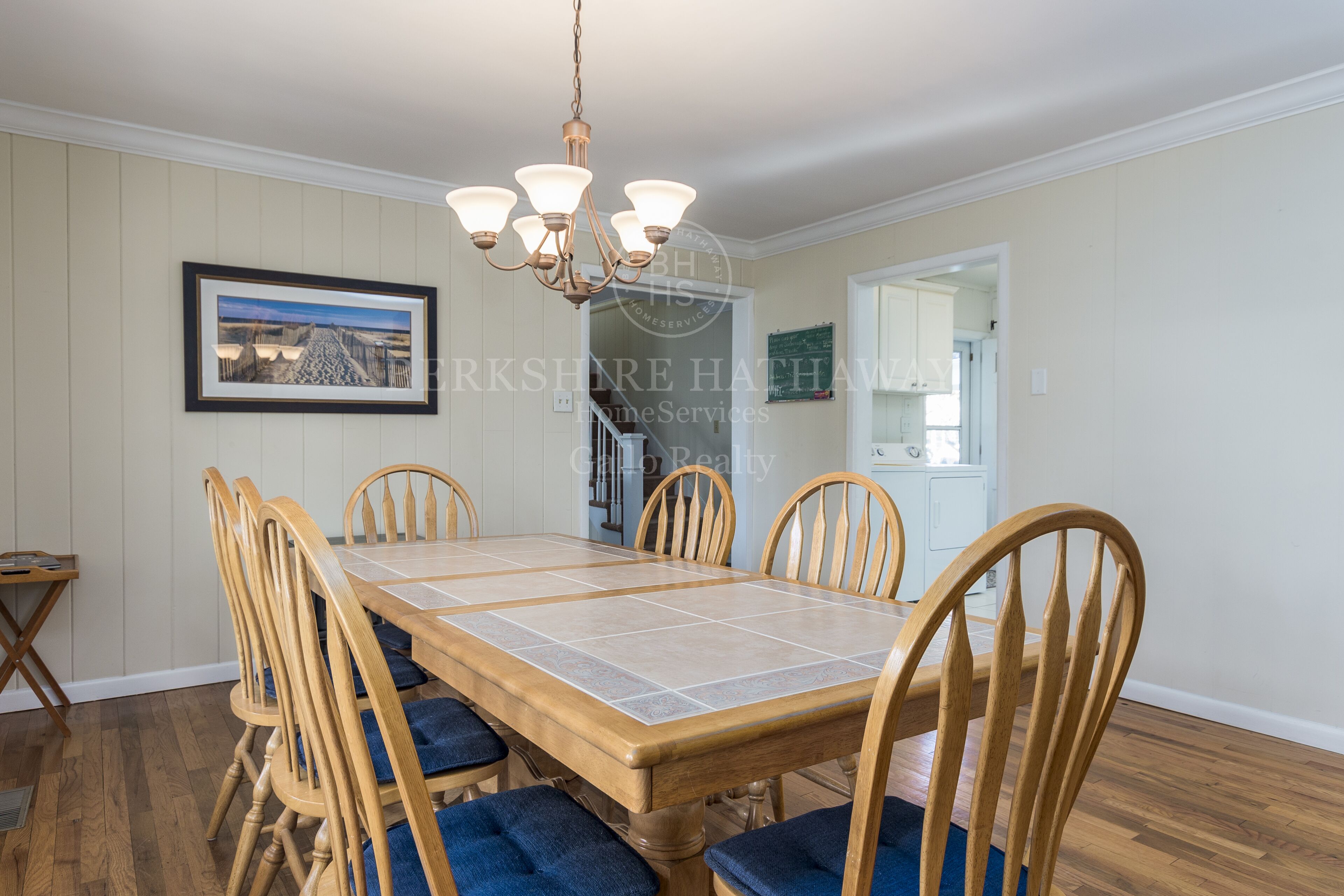 A dining room with a wooden table and chairs, a chandelier, and a framed picture on the wall.