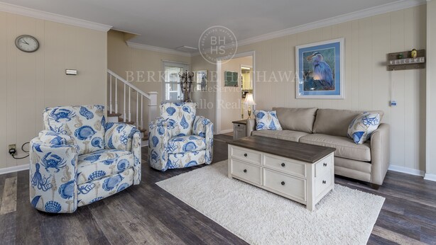 A living room with a beige sofa, two patterned armchairs, a wooden coffee table, and a white rug.