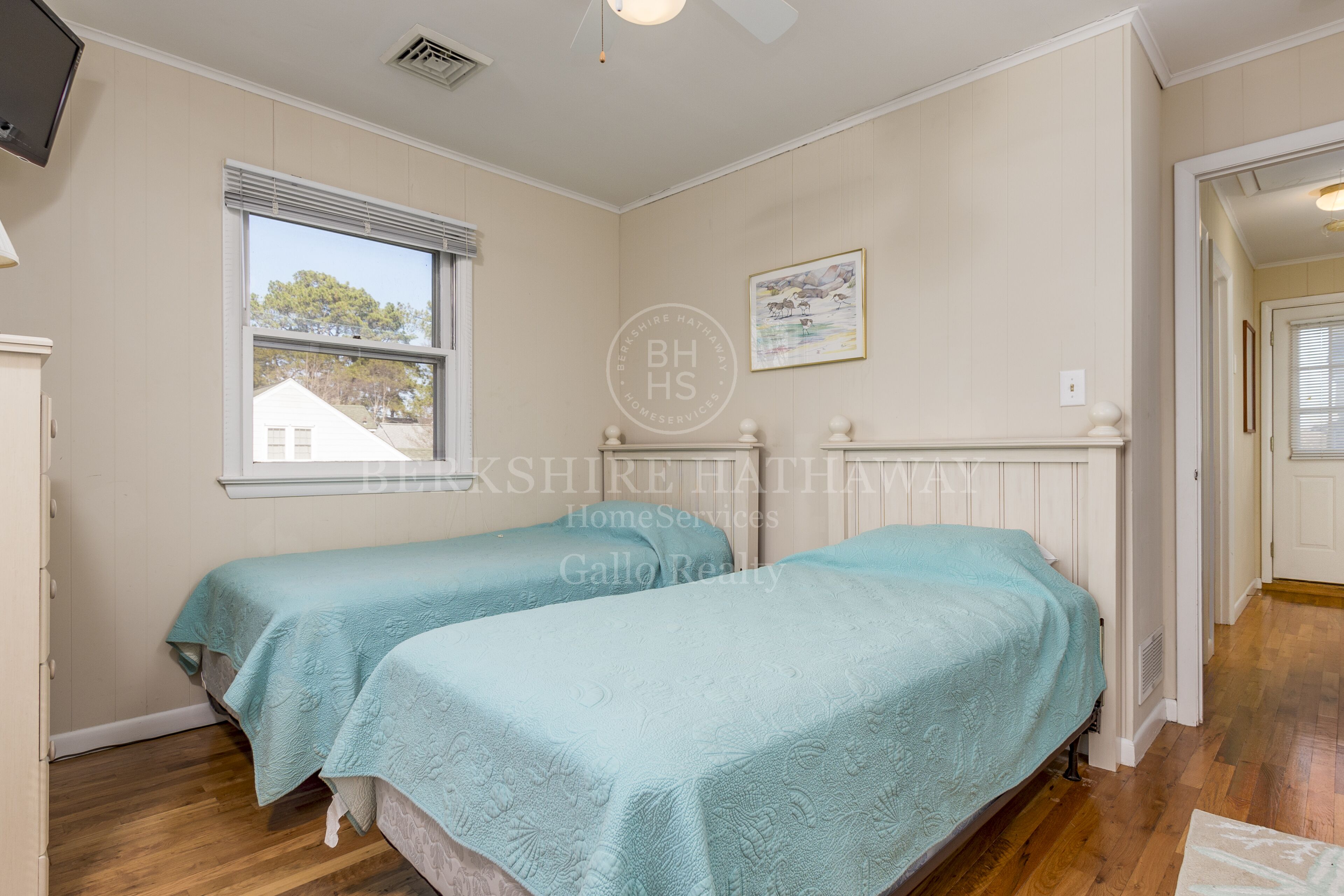 Un dormitorio con dos camas individuales, una ventana, un ventilador de techo y un cuadro en la pared.