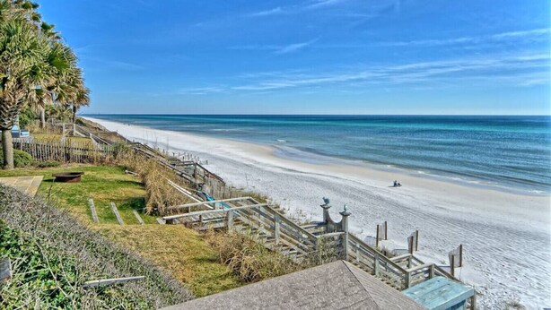 A beach with a wooden staircase leading down to the shore, a clear sky, and a calm sea.