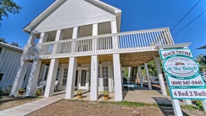 A two-story house with a balcony, a porch, and a sign indicating it is a vacation rental with 4 beds and 2 bathrooms.