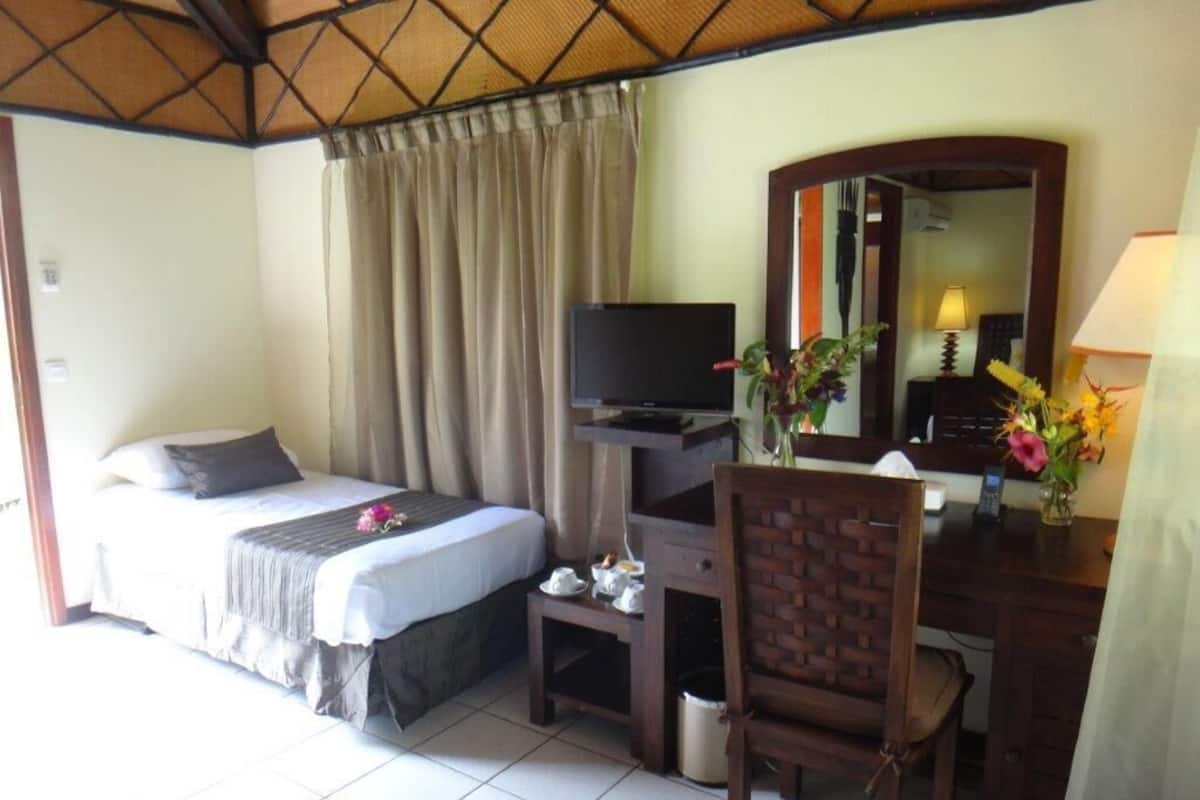 Habitación de hotel con cama, escritorio, computadora, silla, televisor y espejo.