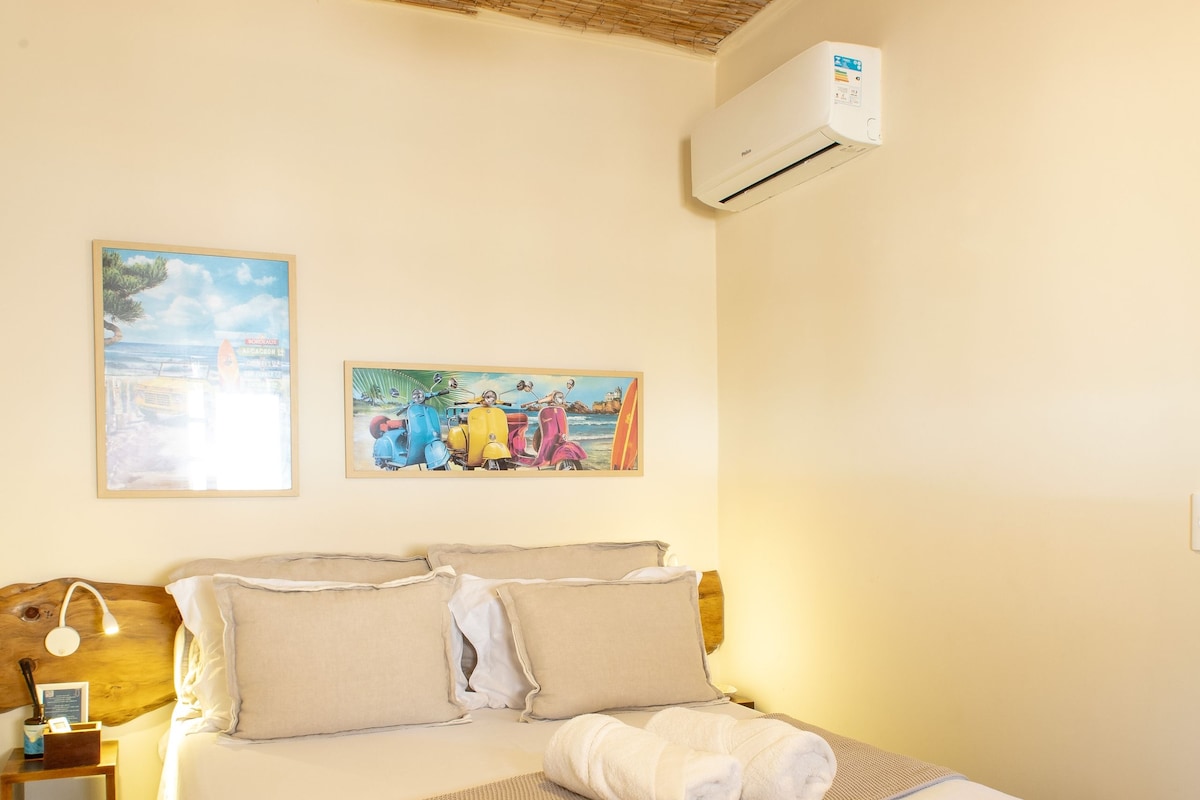A bedroom with a bed, a ceiling fan, an air conditioning unit, and two framed pictures on the wall.