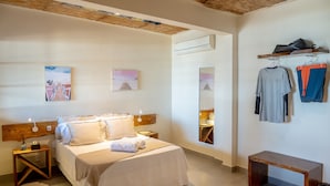 Un dormitorio con cama, mesitas de noche, cabecera de madera, decoración en la pared, equipo de aire acondicionado y perchero.