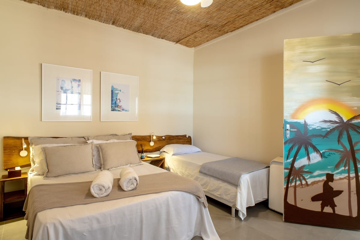 Quarto de hotel com duas camas, um quadro de uma paisagem de praia e teto com textura trançada.