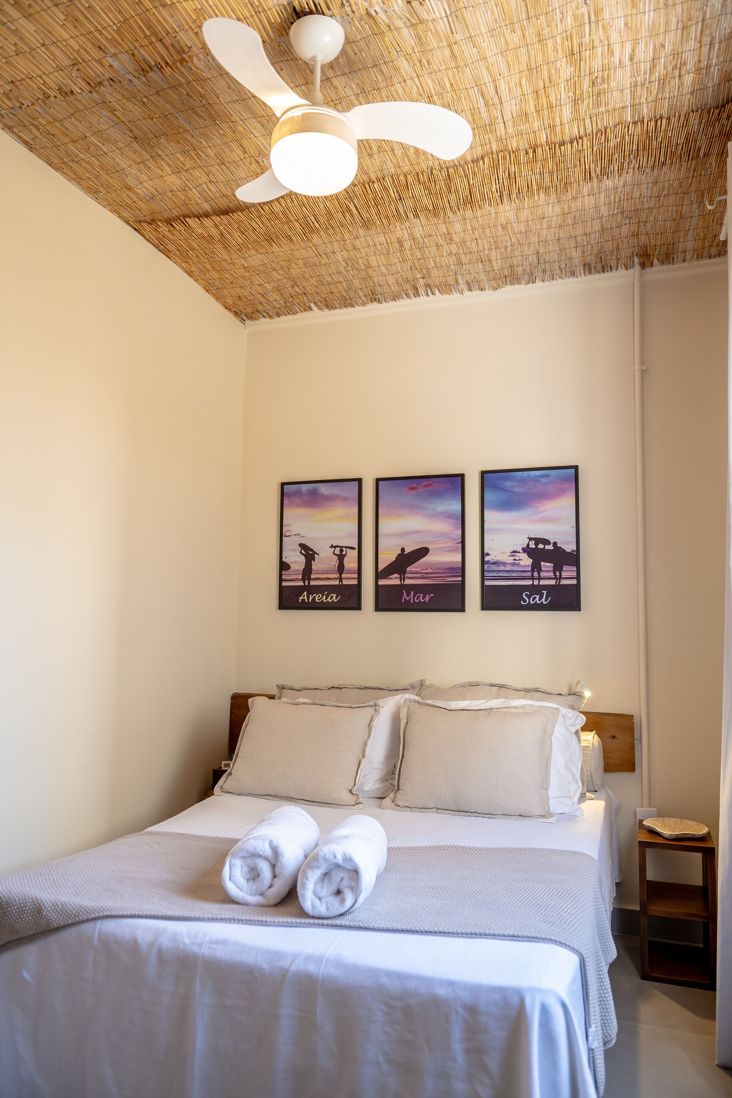 A bedroom with a bed, a ceiling fan, and three framed pictures on the wall.